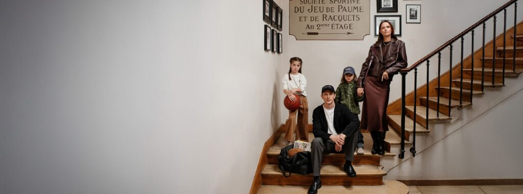 Famille posant dans un escalier avec des tenues IKKS au style urbain et sophistiqué, ambiance rétro chic avec panneau mural indiquant